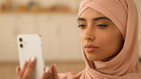 Serious Muslim woman Islamic girl ethnic female in hijab indoors at home using mobile phone typing chatting smartphone shopping online app social media technology delivery order purchase internet smsの写真素材