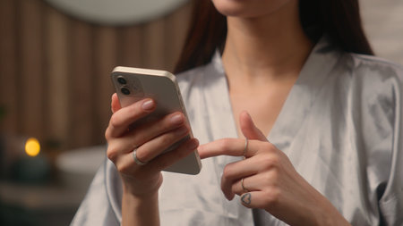 Close up cropped view at home bathroom woman female hands lady girl indoor using mobile phone online smartphone internet web net cellphone social media app browsing chatting shopping buying cosmeticの写真素材