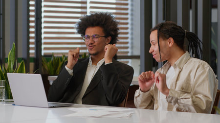 Two African American men businessmen business males guys colleagues in office partnership cooperation win victory celebrate online internet achieve success dancing winning laptop computer good resultの写真素材