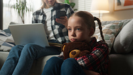Caucasian family upset lonely kid girl suffering busy mother woman using laptop working from home ignoring child daughter holding Teddy Bear parenting ignore lack of attention childcare trouble stressの写真素材