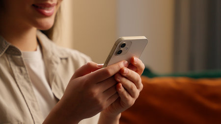 Close up cropped view Caucasian happy smiling user woman girl female lady using mobile phone apps typing message in internet modern technology net at home in living room smartphone online chattingの写真素材