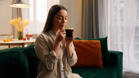 Happy relaxed peace dreamy woman calm female girl lady at home drinking coffee morning drink aroma black tea holding cup of beverage dreaming thinking weekend resting in living room mortgage insuranceの写真素材