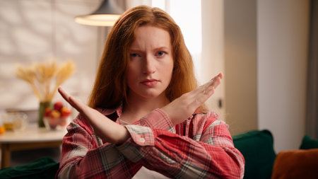 Woman crossed arms stop no gesture not forbidden gesture shaking head no at home girl negative answer looking at camera indoors Caucasian female crossing hands deny in living room end symbol finishの写真素材