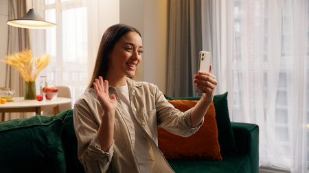 Caucasian happy smiling user woman girl female lady using mobile phone record video call conference chat blog vlog influence apps talking to smartphone web camera internet modern technology at homeの写真素材