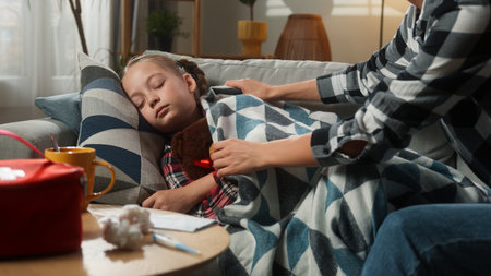 Caucasian family at home ill sick sleeping kid girl daughter mother woman mom cover child with blanket touching forehead checking temperature fever childcare health problem medicine symptom pandemicの写真素材