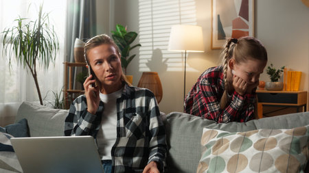Caucasian family stress busy mother working laptop at home noisy child disturb pick up mobile phone woman mom talking call noisy upset offended kid daughter girl freelancer trouble lack of attentionの写真素材