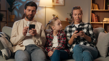 Caucasian family parents mother father using mobile phone smartphones scrolling gadgets addict dependence internet ignore daughter child sad kid girl ask attention lonely problem at evening home nightの写真素材