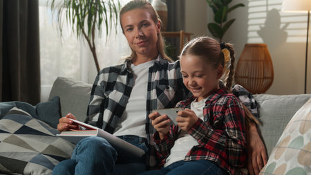 Caucasian family at home living room little girl child kid daughter gadget addict dependency addiction mobile phone smartphone video game playing ignore mother woman trying reading book offering shrugの写真素材