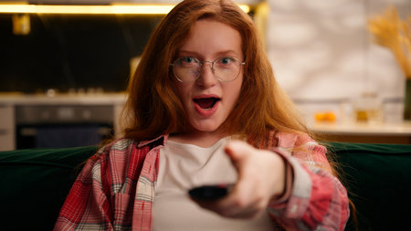 Teen girl relaxing at home living room weekend Caucasian woman female rest on couch holding bowl with popcorn snack switch channels choose TV program emotional reaction choosing movie cinema seriesの写真素材