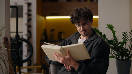 Concentrated Hispanic guy reading literature holding book at home hipster turning page focused smart adult man reader male looking text poetry relaxing enjoying novel hobby read story library leisureの写真素材
