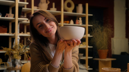 Smiling Caucasian woman girl female artist sculptor artisan potter small business owner saleswoman holding bowl ceramics modeling clay handmade pottery workshop art studio sell handmade craft artworkの写真素材