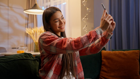 Caucasian woman teenager girl blogger photo selfie mobile phone at evening home female blogger influencer holding smartphone camera photograph stylish picture online blog social media video contentの写真素材