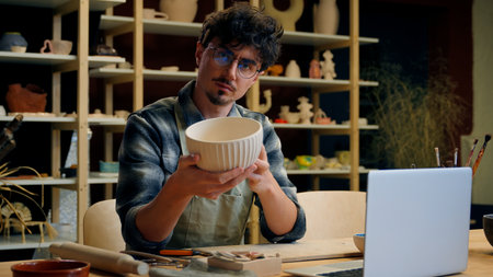 Caucasian man sculptor potter online laptop shopping in pottery workshop create handmade ceramics small business owner sale craft art male guy craftsman designer sell handcraft bowl crockery stonewareの写真素材
