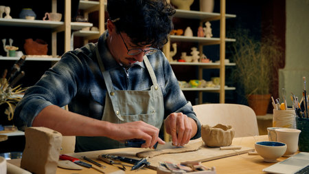 Concentrated man Caucasian male guy artist sculptor craftsman potter small business owner process modeling handcraft pottery workshop create handmade eco ceramics cutting clay material in art studioの写真素材