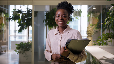 Portrait ethnic African American business woman indoors entrepreneur businesswoman ceo employer manager executive consultant with documents looking at camera smile cheerful happy girl in office jobの写真素材