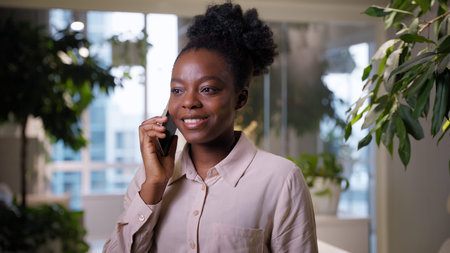 Smiling business woman African American ethnic girl businesswoman talking mobile phone in office...