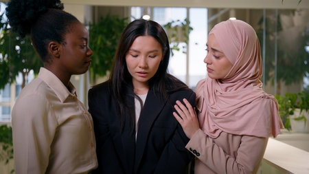 Upset sad frustrated crying Asian girl in office dismissed lost job crisis women business colleagues African Muslim businesswomen support help calm multiracial friendship community supportive unityの写真素材