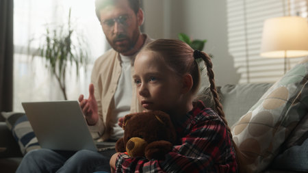 Caucasian family at home remote working dad using computer on sofa speaking to sad little girl child kid cuddling Teddy Bear conflict emotional stress childhood problem loneliness attention deficitの写真素材