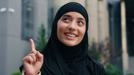 Portrait happy smiling Muslim business woman Islamic businesswoman girl female in black hijab employer in city showing one finger come up with idea solution decision pensive dreaming thinking outdoorsの写真素材