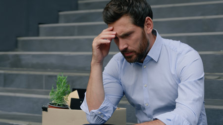 Close up depressed Caucasian middle aged business man lost job pensive holding head frustrated emotion sitting stairs near office building with dismissal box businessman male suffering unemploymentの写真素材