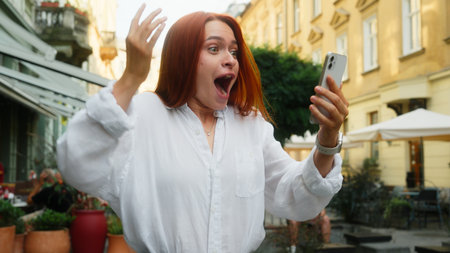 Happy joyful woman girl female winner student businesswoman excited lady in city hold mobile phone gadget addict amazing news victory shock surprise celebrate success online money win prize outdoorsの写真素材