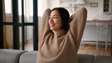 Hispanic woman relaxed calm girl lady homeowner sit on couch at home happy smiling female put hands behind head relax rest on sofa enjoy comfort lazy break casual weekend leisure alone air conditionerの写真素材