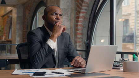 African American ethnic adult employer entrepreneur thinking problem solution hesitate decision ponder think come up with idea man business office businessman male manager guy at table typing laptopの写真素材