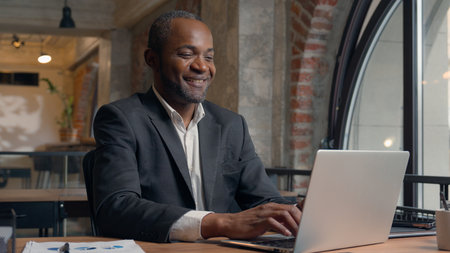 African American middle-aged entrepreneur smiling happy laughing positive typing laptop computer ethnic business man office businessman smile male guy working with pc online job chatting with clientの写真素材
