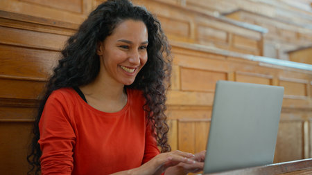 Smiling happy positive Latina woman smile looking at camera student girl female typing laptop online e-learning education using internet preparing to exam in university college auditorium studyingの写真素材