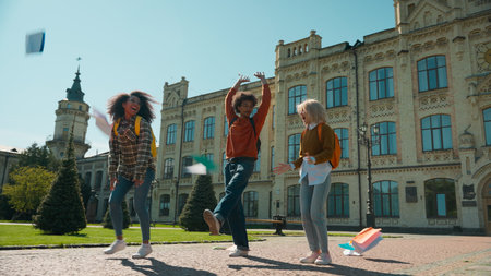 Three multiracial students girls African American women Caucasian female ladies boy man guy male leave college university high school talking walking in city throwing books celebrate education breakの写真素材
