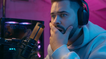 Portrait close up Caucasian man male gamer guy streamer online video game addict computer e-sport cyber gaming in headphones with microphone at night neon light indoors upset frustrated lost failureの写真素材