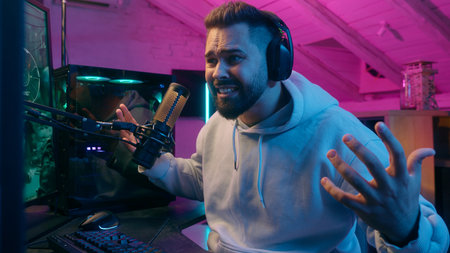 Smiling Caucasian man guy male gamer streamer playing online game at night lost upset frustrated angry mad furious with bad result failure addiction streaming in neon room player bangs fists on tableの写真素材