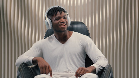 Futurism African American man male guy in white futuristic room indoors cyberspace modern technology in wireless headphones listening music listen song audio relaxing in chair dancing enjoy soundの写真素材