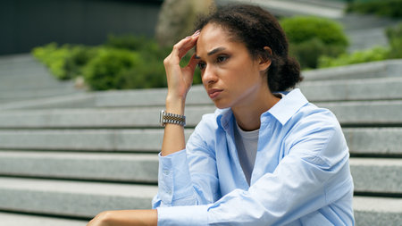 Tired troubled stressed African American businesswoman business woman girl female worker employer anxiety suffering in city sitting on stairs headache pain migraine unemployment crisis problem ladyの写真素材