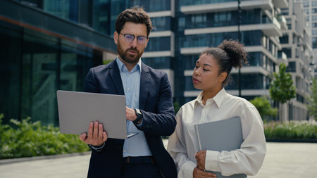 Multiracial business people walk in city multiethnic colleagues Caucasian businessman man male guy African woman businesswoman girl female discuss laptop online data looking computer talk go outsideの写真素材