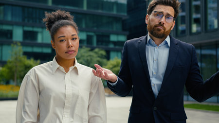 Two sad upset multiethnic coworkers business colleagues managers Caucasian man businessman male guy African American woman businesswoman female girl failure in city spread hands sides shrug shouldersの写真素材