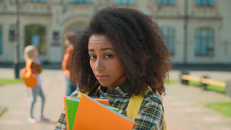 Sad upset stressed disappointed African American student girl female woman lady teen teenager standing alone in city outdoors university college high school suffer bullying talking students backgroundの写真素材