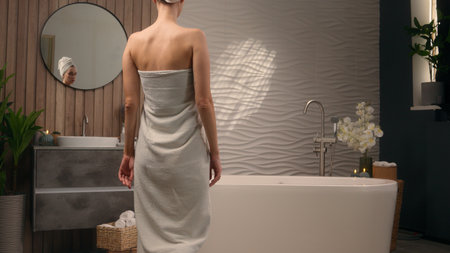 Back view Caucasian female woman lady girl wrapping in white cotton towel take off preparing for bathing ready for washing in bath tub in home bathroom beauty procedure body care routine relaxing spaの写真素材