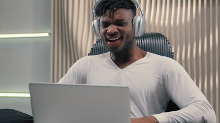 African American ethnic cyber man in white futurism studio indoors business male user gamer hacker businessman guy futuristic in headphones win laptop success achieve computer good news amazed wowの写真素材