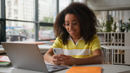 African American girl student gadget addict using mobile phone chatting social media looking in...
