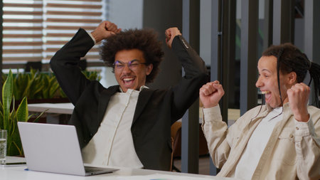 Two African American men guys multiracial multiethnic male businessmen business coworkers colleagues co-workers looking at laptop in office work achieve winning result victory celebrate growth luckの写真素材