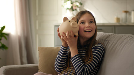 Little girl shake piggy bank saving money finance cash investment childhood budget child kid pupil smiling delighted rejoice enjoy coins capital account economic fund wealth deposit currency rich homeの写真素材