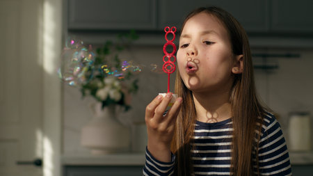 Little girl blowing soap bubbles childhood playful child daughter kid home air joy playing soapy fun...