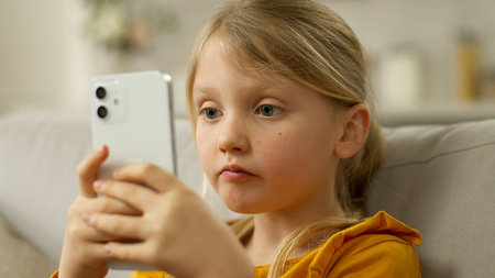 Little European girl holding mobile phone smartphone cellphone surprised wow shocked unexpected...