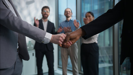 Close up handshake two businesspeople shaking hands background of office multiethnic workers applause businessmen businesswomen team successful business financial deal agreement partners cooperationの写真素材