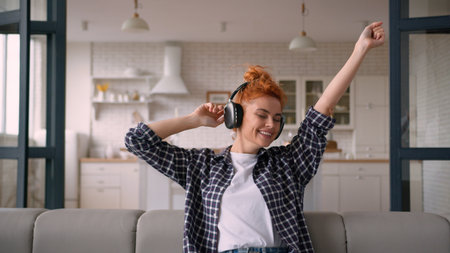 Happy funny moving dancing joyful Caucasian woman girl female at home couch weekend enjoy dance listening music in wireless headphones earphones listen song audio sound move relaxing on sofa joy funの写真素材