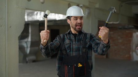 Builder emotional man Caucasian guy engineer repairman holding hammers tools repair work industry architect in hard hat male foreman on construction site building smiling handyman repairman posingの写真素材