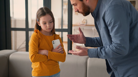 Irritated Caucasian father man parent scolding talk guilty device addicted little child girl daughter kid family problem quarrel offend. Angry dad male take away mobile phone punishment argument homeの写真素材