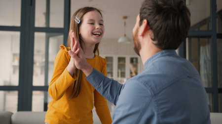 Playful carefree Caucasian family father man daddy male giving high five child girl clap touching parent dad daughter holding hands little kid schoolgirl smiling laugh good job gesture success at homeの写真素材