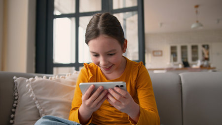 Cheerful glad Caucasian little kid touching mobile phone smartphone screen gaming girl winning smile...
